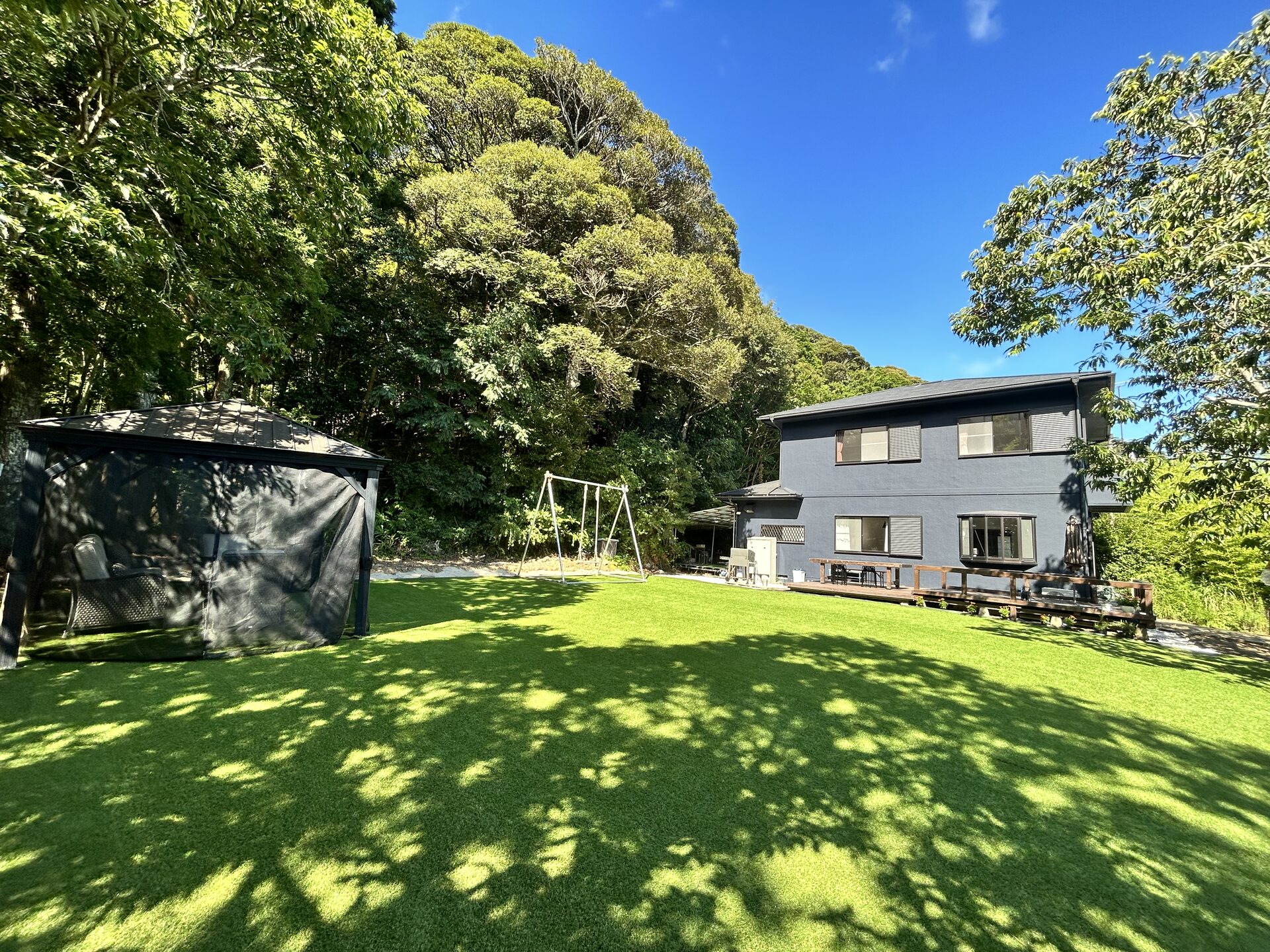 BlueFlow KATSUURA's main house exterior on a sunny day, with a spacious garden featuring a gazebo and swing